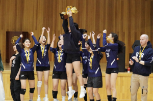 The varsity girls erupt in cheers, proudly wearing their medals as they hoist the championship trophy high. Their faces glow with pride and excitement, celebrating the triumph of a season built on hard work and teamwork.
